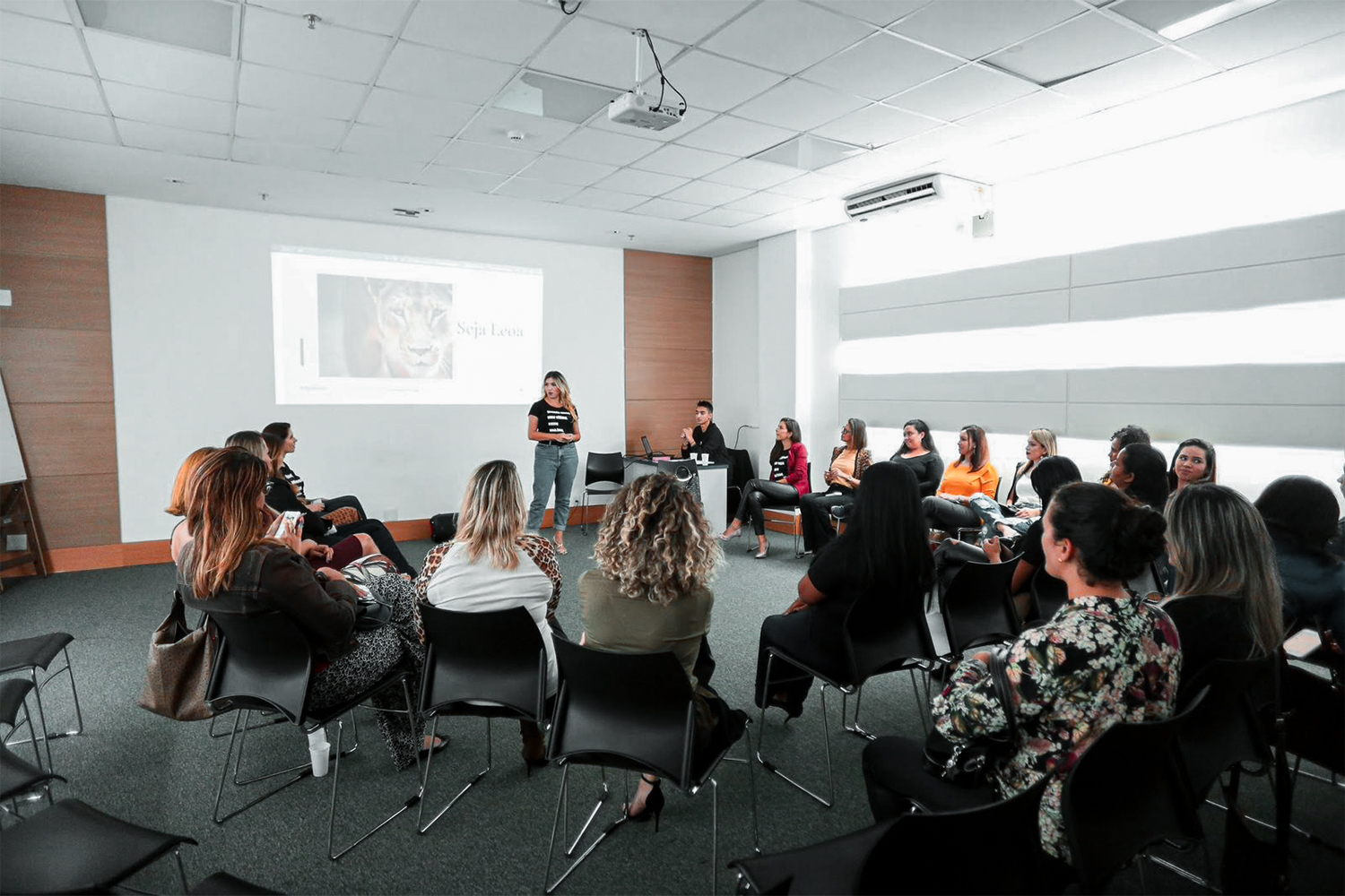 Liza Lopes apresentando um encontro para um grupo de mulheres sentadas em auditório