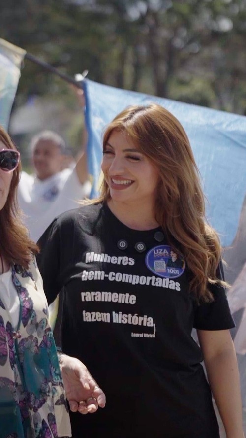 Liza Lopes caminhando de mãos dadas com uma apoiadora durante ato de rua
